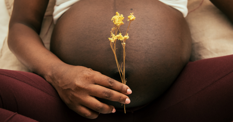 A woman holds flowers in front of her pregnant belly