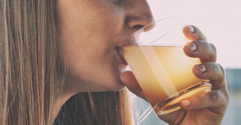 a woman sips from a glass of brown, dirty drinking water