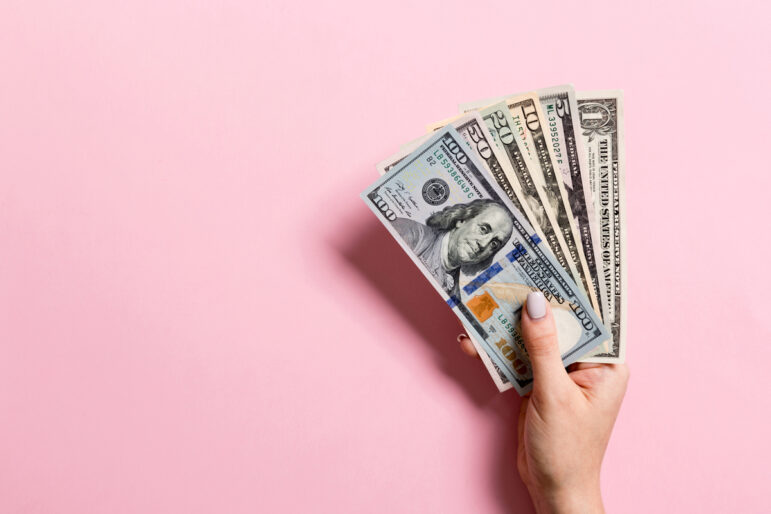 a woman's hand holds up cash on a pale pink background