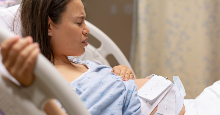 A pregnant woman site in her hospital bed, clutching the siderails as she takes a deep breath