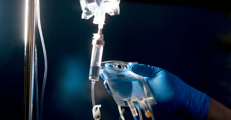 Gloved hand lifting up bag of medication for infusion