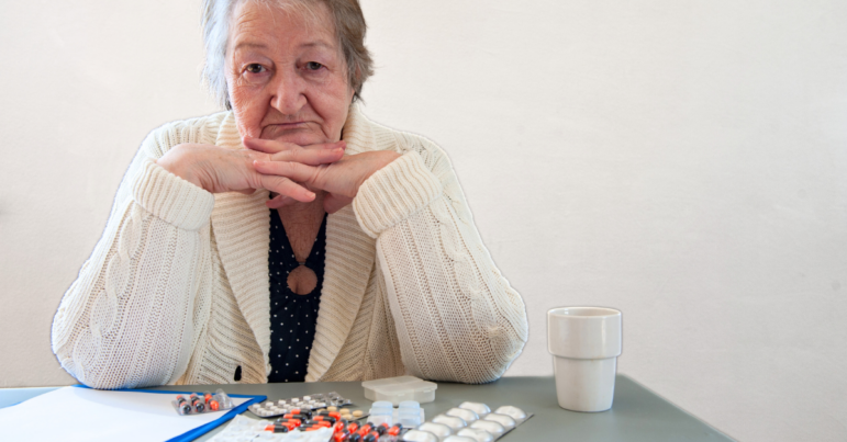 an older woman looks into the camera with a spread of medications in front of her